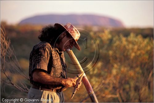 AUSTRALIA CENTRALE - Uluru Kata Tjuta National Park - un aborigeno suona i "didgeridoo", strumento musicale tradizionale - sullo sfondo il Ayres Rock